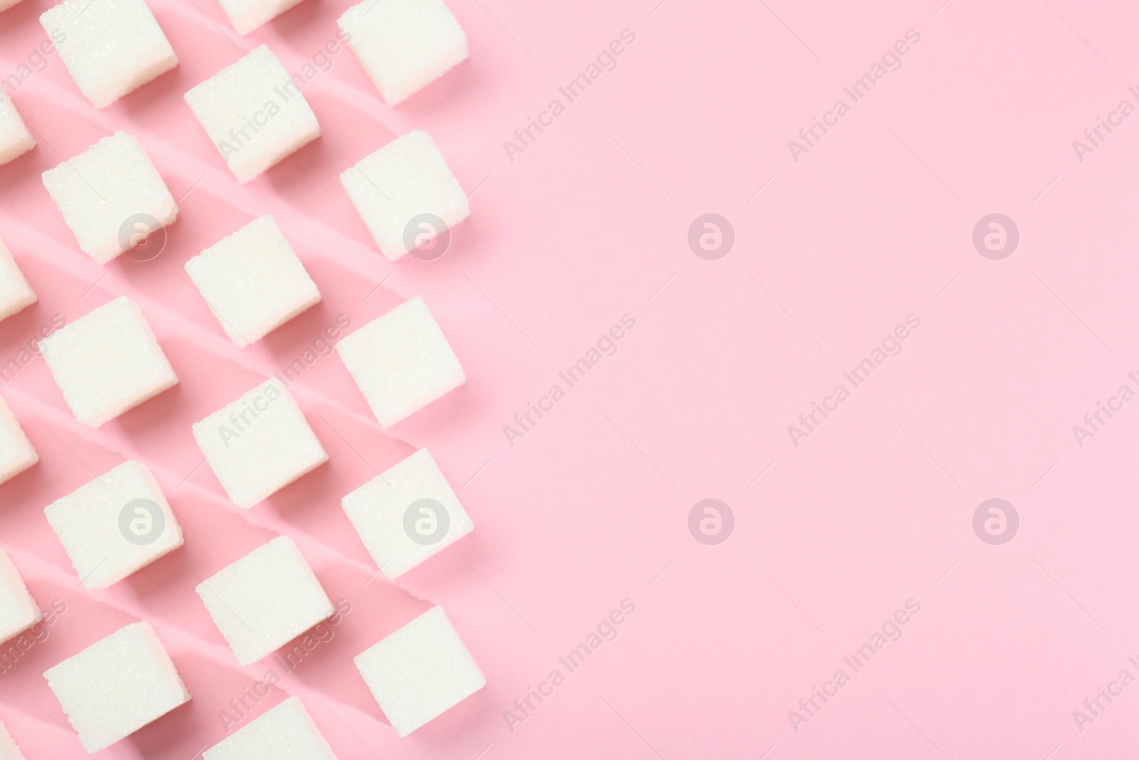 Photo of White sugar cubes on pink background, top view. Space for text