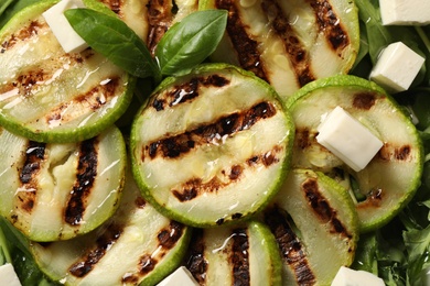 Photo of Delicious grilled zucchini slices and feta cheese as background, top view