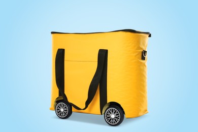 Image of Yellow thermo bag on wheels against light blue background. Food delivery service