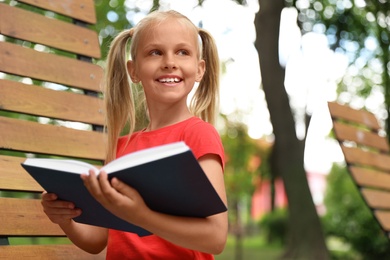 Image of Happy little girl reading book in park 