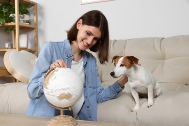 Photo of Woman pointing at globe near dog in room. Travel with pet concept