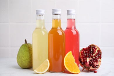 Delicious kombucha in glass bottles and fresh fruits on white marble table