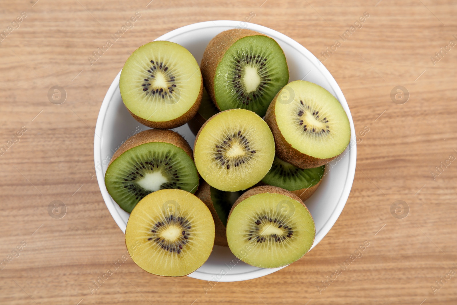 Photo of Bowl of many cut fresh kiwis on wooden table, top view