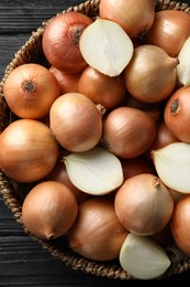 Whole and cut onions on black wooden table, top view