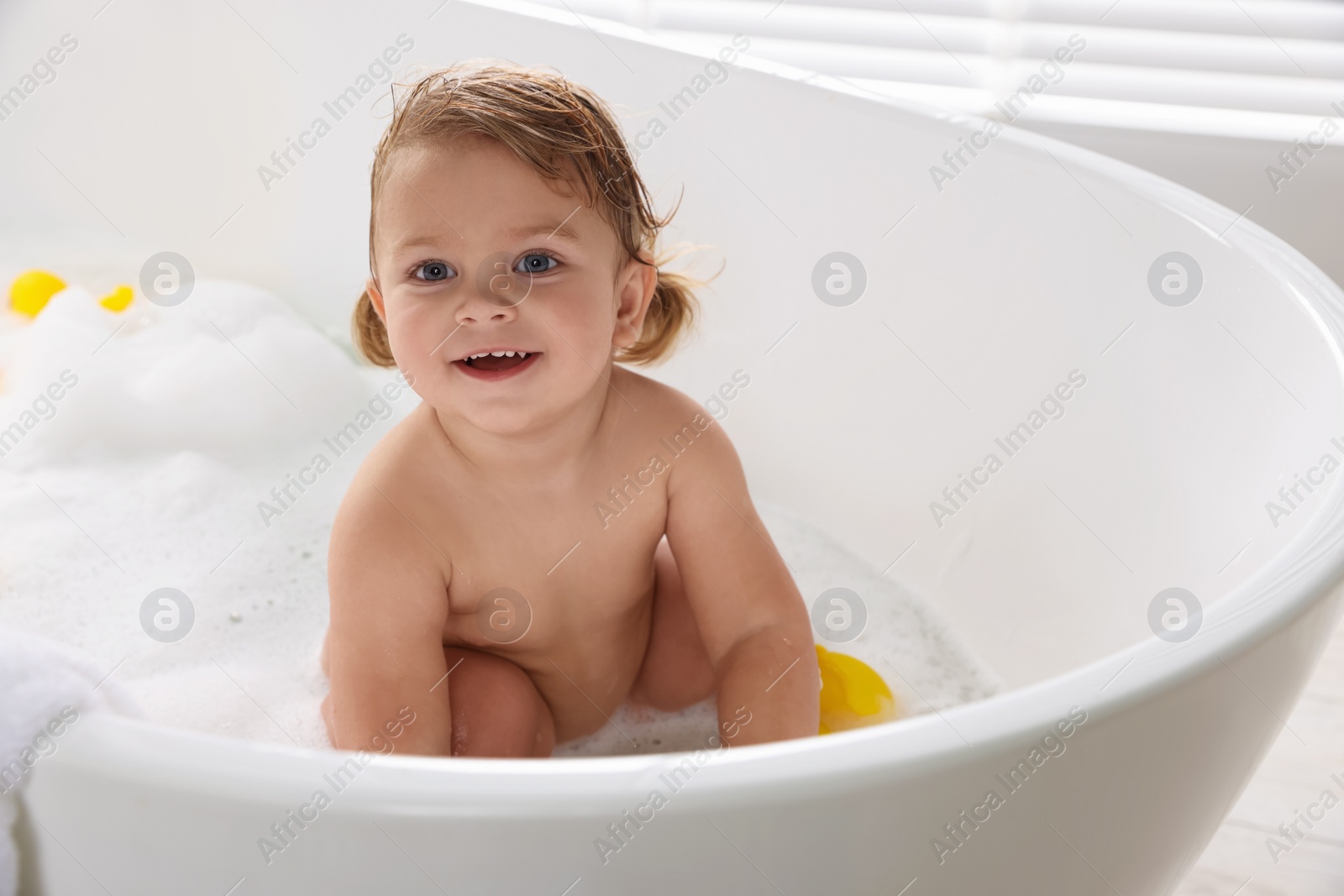 Photo of Cute little girl taking bubble bath with toys indoors