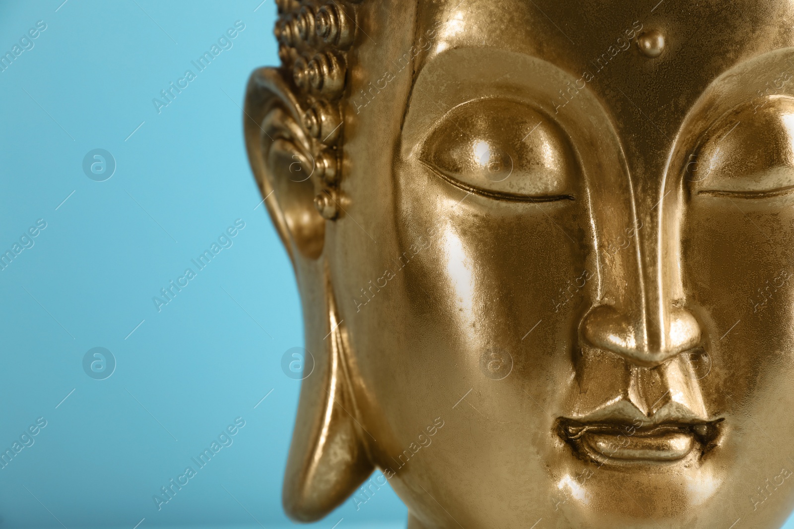 Photo of Beautiful golden Buddha sculpture on light blue background, closeup. Space for text