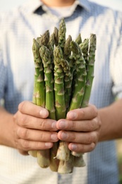 Photo of Man holding fresh raw asparagus outdoors, closeup