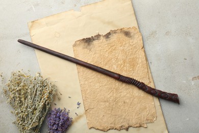 Photo of Magic wand, dry flowers and old papers on light textured background, flat lay