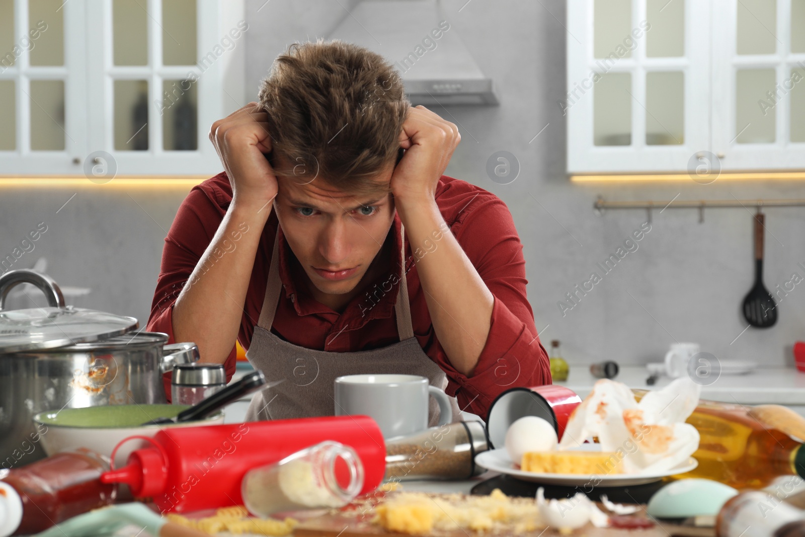 Photo of Upset man in messy kitchen. Many dirty dishware, utensils and food leftovers on table