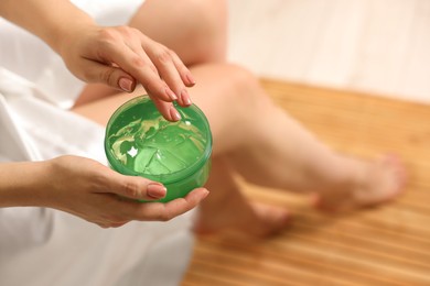 Photo of Young woman holding jar of aloe gel indoors, closeup. Space for text
