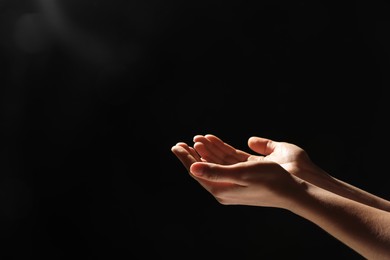 Photo of Religion. Woman with open palms praying on black background, closeup. Space for text