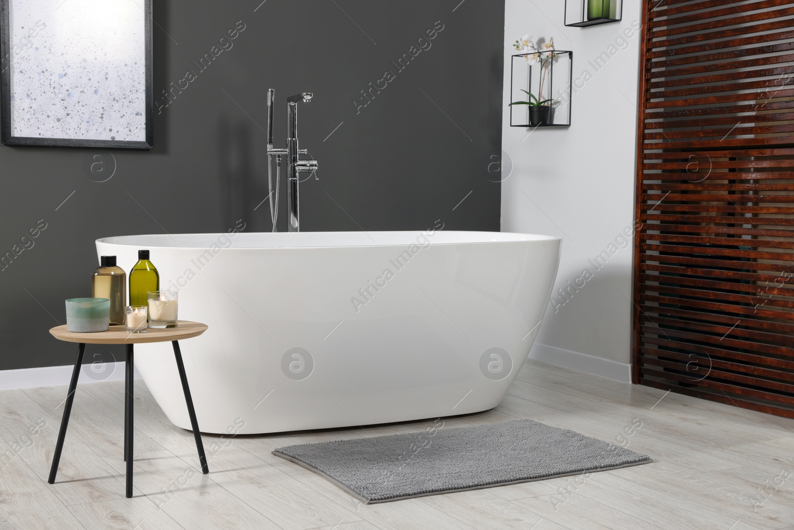 Photo of Stylish bathroom interior with ceramic tub and care products on coffee table