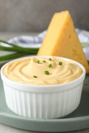 Photo of Tasty cheese sauce with green onion in bowl on plate, closeup