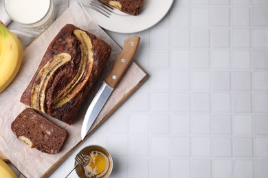 Photo of Delicious banana bread served on white tiled table, flat lay. Space for text