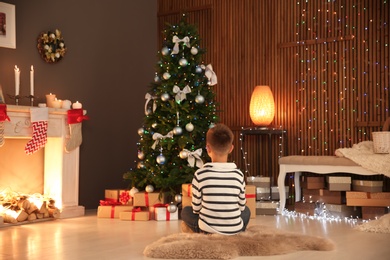 Cute little child sitting near Christmas tree at home