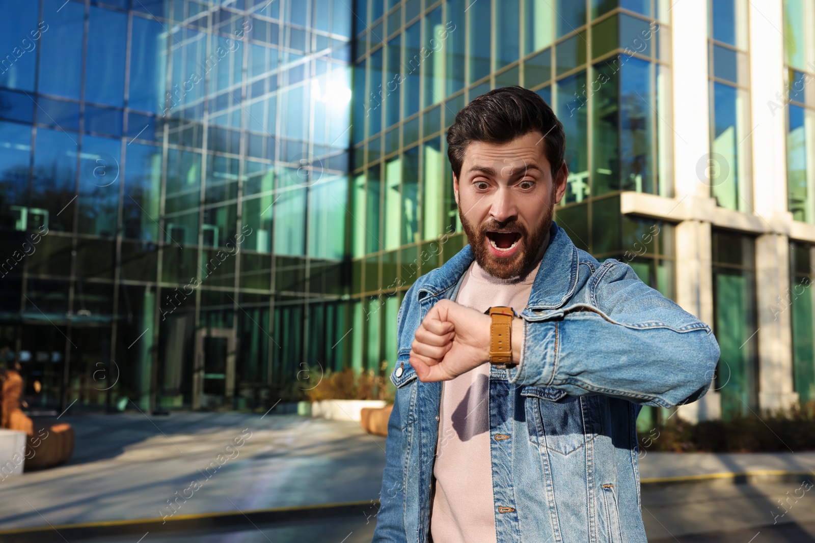 Photo of Emotional man checking time on watch near building. Being late concept