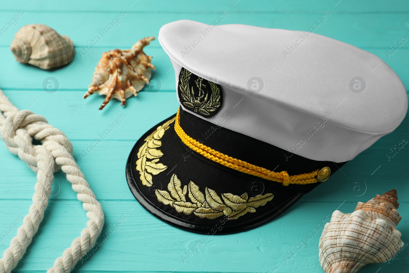 Photo of Peaked cap, rope and shells on turquoise wooden background