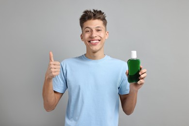 Photo of Young man with mouthwash showing thumbs up on light grey background