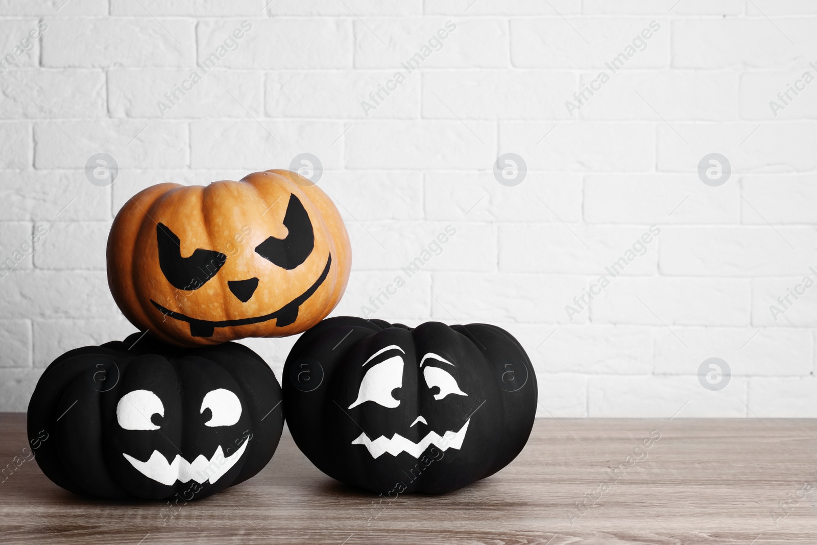 Photo of Pumpkins with scary faces near brick wall, space for text. Halloween decor