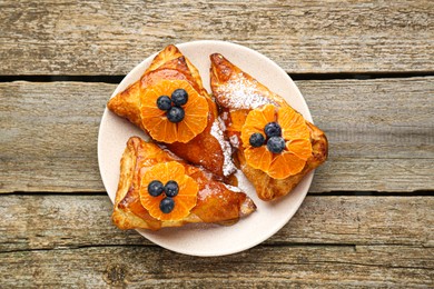 Fresh tasty puff pastry with sugar powder, jam, tangerines and blueberries on wooden table, top view