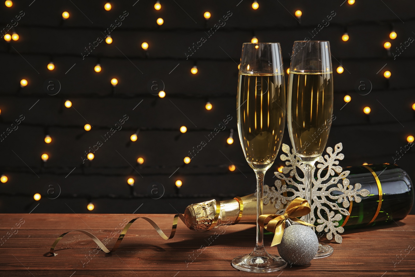 Photo of Glasses of champagne with bottle and festive decor on table against blurred fairy lights