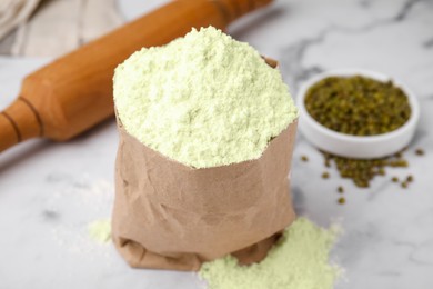 Photo of Mung bean flour in paper bag and seeds on white marble table