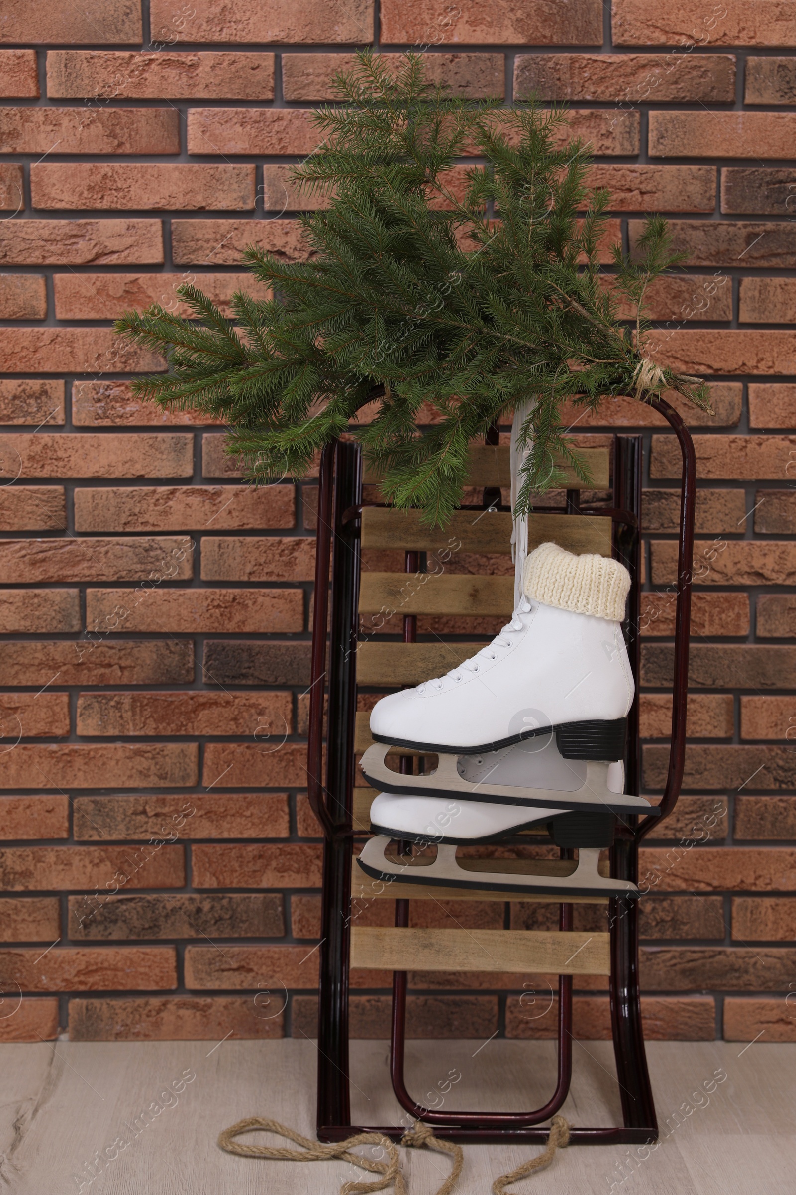 Photo of Sleigh with pair of ice skates and fir branches near brick wall indoors
