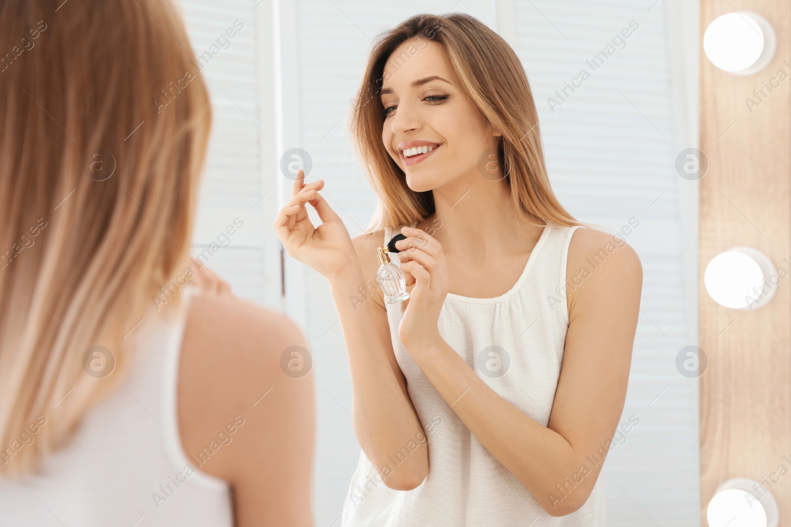 Photo of Young woman applying perfume near mirror indoors