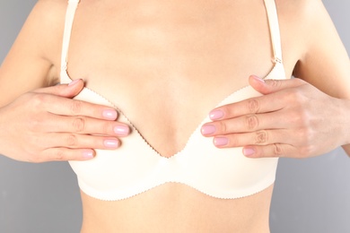 Photo of Young woman in white bra on gray background, closeup. Breast cosmetic surgery