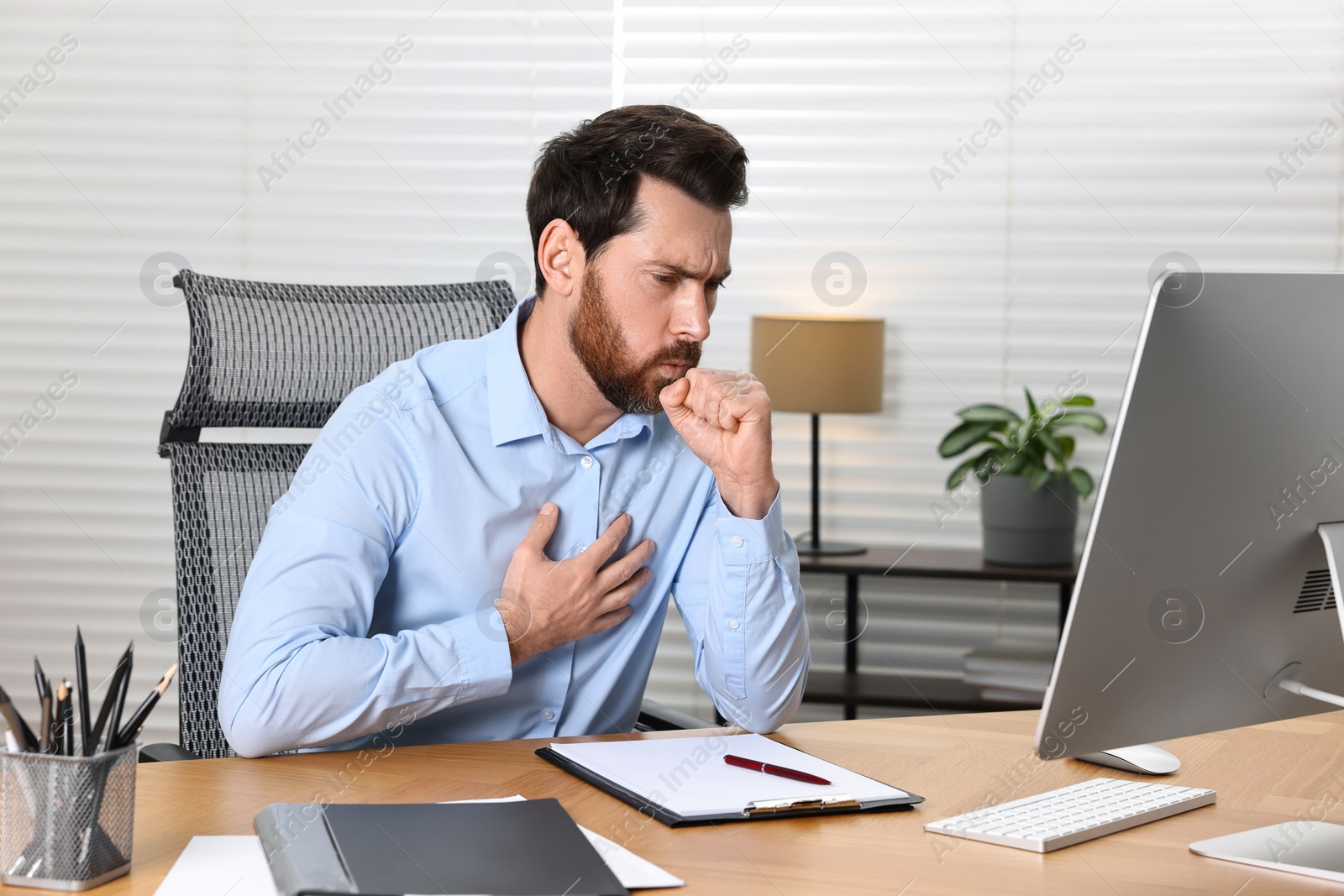 Photo of Sick man coughing at workplace in office. Cold symptoms