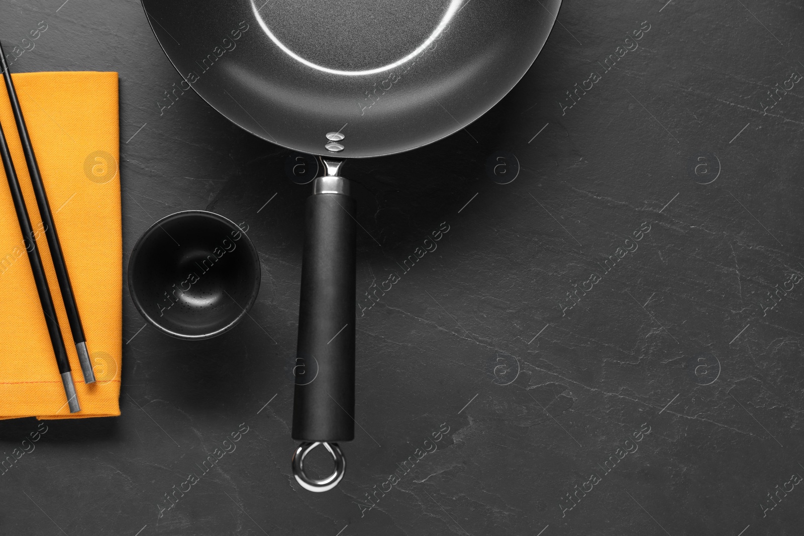 Photo of Empty iron wok, sauce bowl and chopsticks on black table, flat lay. Space for text