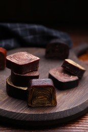 Photo of Many tasty chocolate candies on wooden board