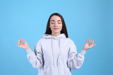 Photo of Young woman meditating on light blue background. Stress relief exercise