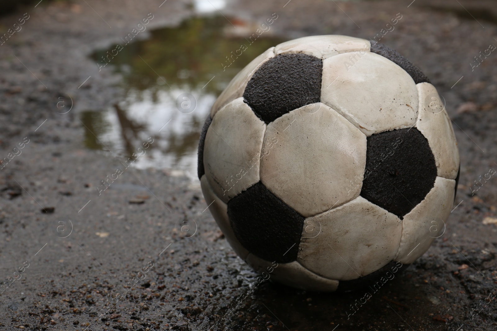 Photo of Dirty soccer ball near puddle on ground, closeup