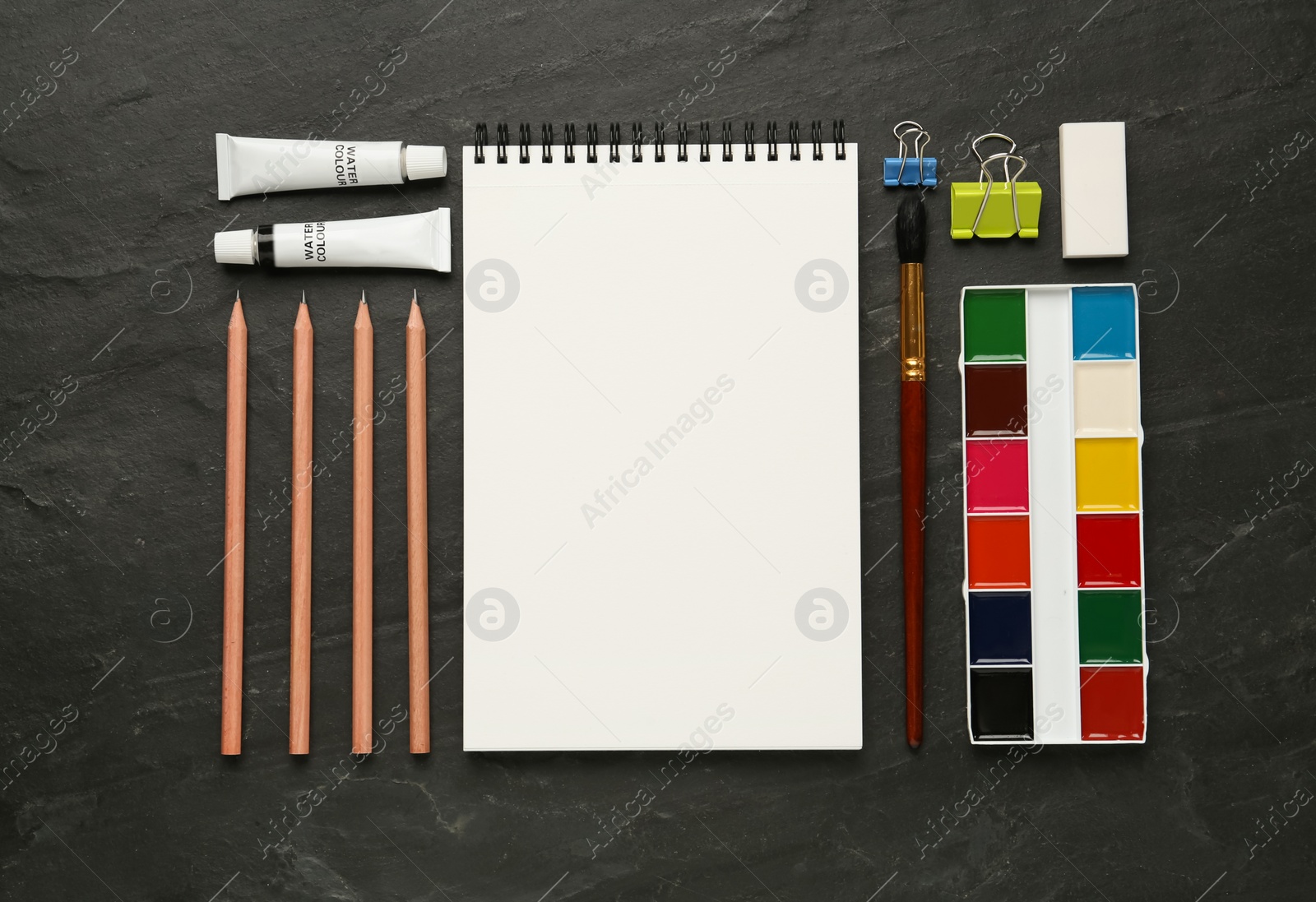 Photo of Flat lay composition with blank sketchbook on black slate table. Space for text