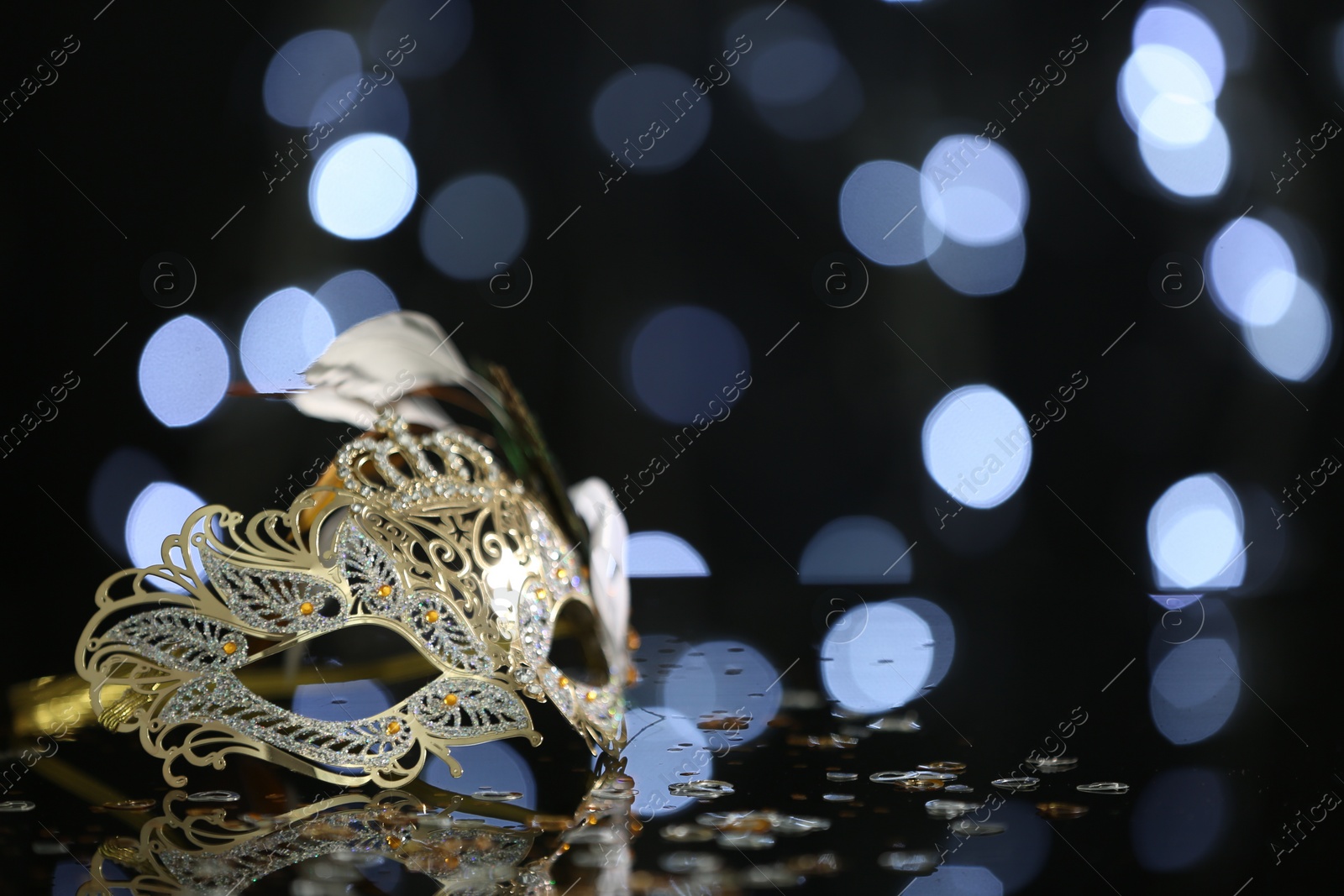 Photo of Beautiful carnival mask on table against blurred lights. Space for text