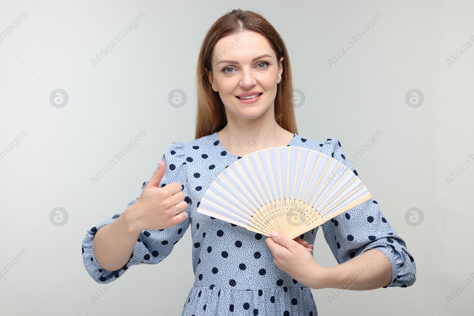 Photo of Happy woman with hand fan showing thumb up on light grey background