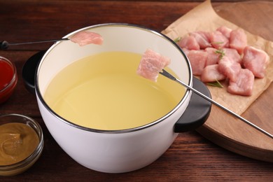 Fondue pot, forks with pieces of raw meat and sauces on wooden table, closeup