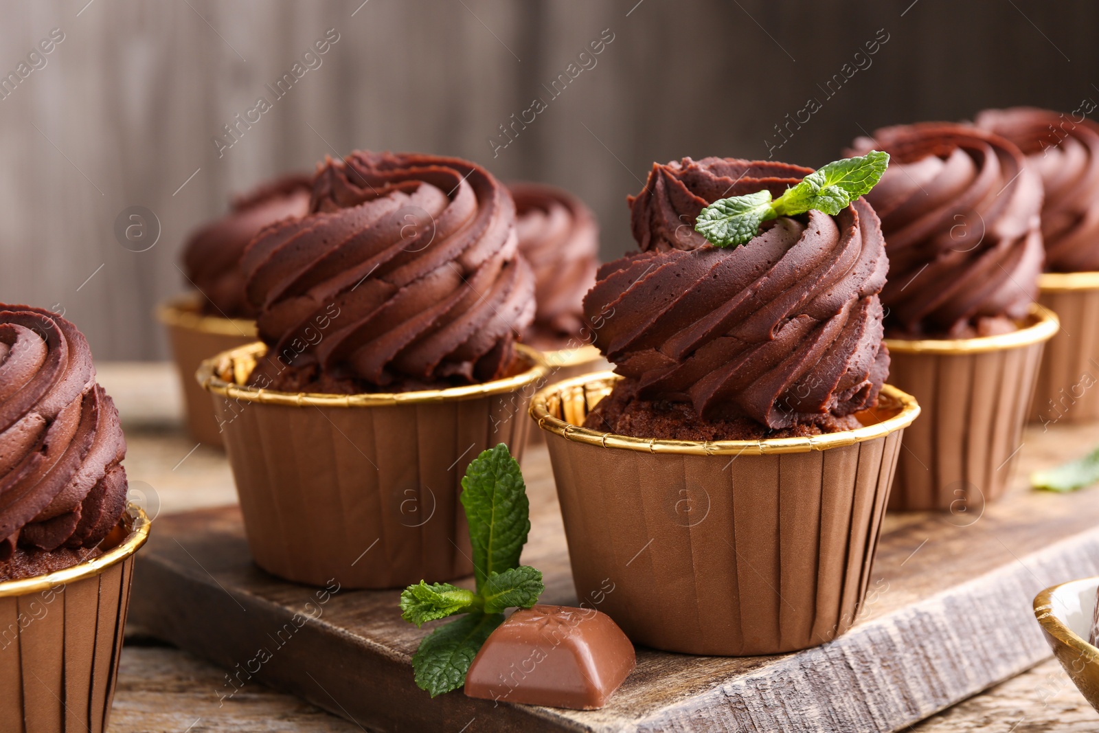 Photo of Delicious cupcakes with chocolate pieces and mint on wooden table, closeup