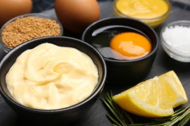 Photo of Delicious homemade mayonnaise and ingredients on black table, closeup