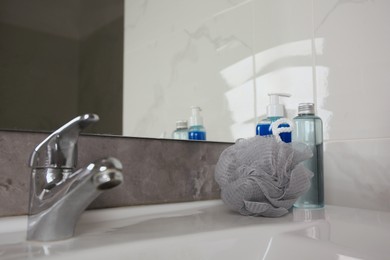 Grey shower puff and cosmetic products on washbasin in bathroom