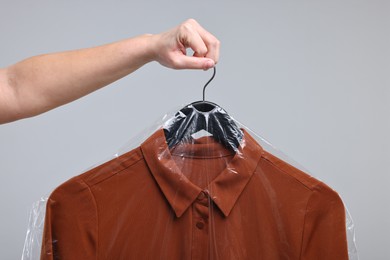 Dry-cleaning service. Woman holding shirt in plastic bag on gray background, closeup