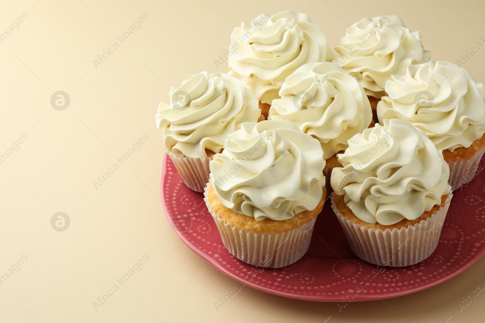 Photo of Tasty vanilla cupcakes with cream on beige table. Space for text