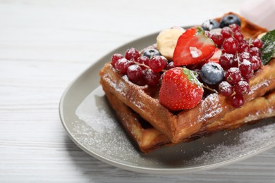 Photo of Plate of delicious Belgian waffles with berries and powdered sugar on white wooden table, closeup