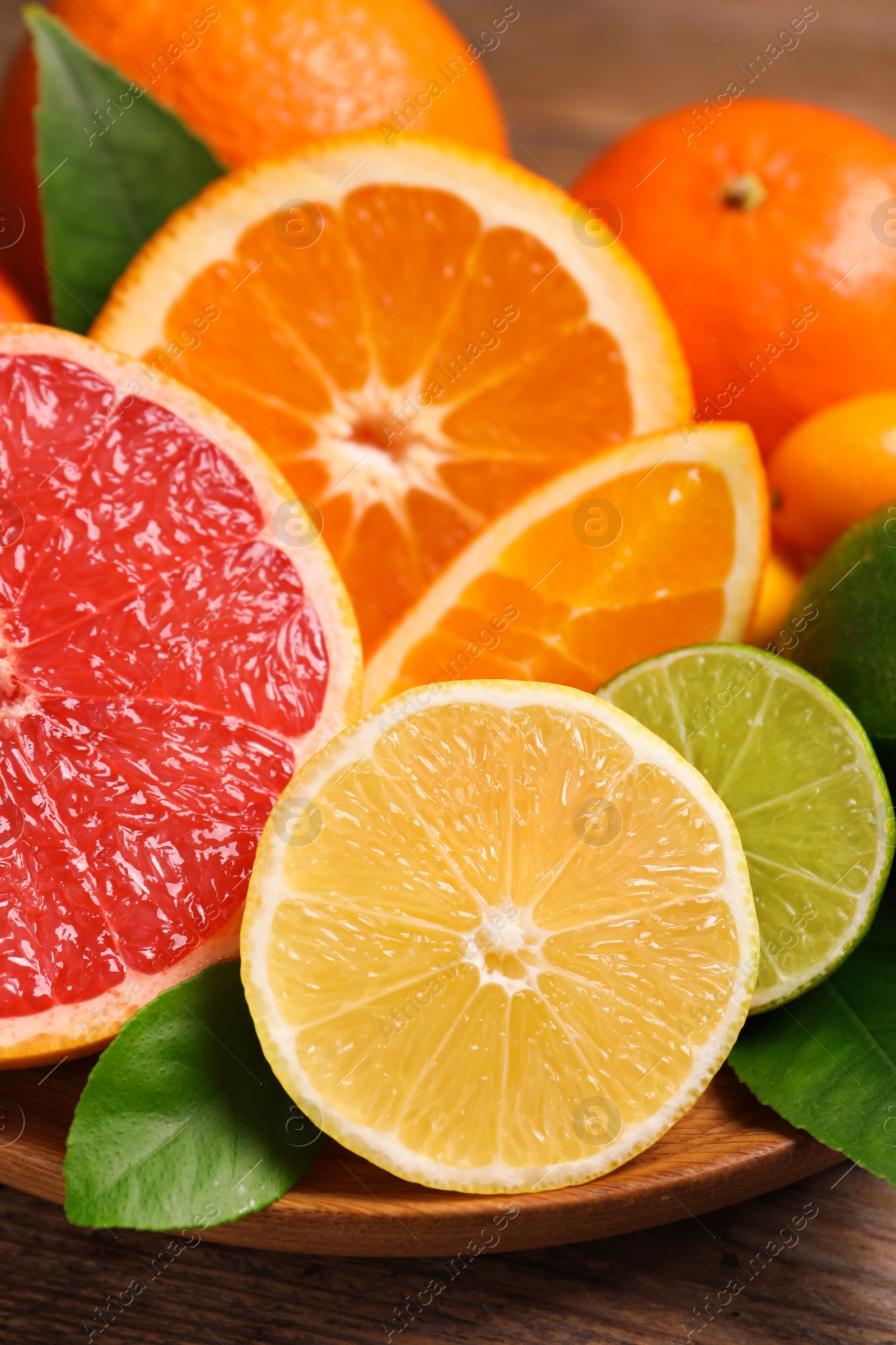 Photo of Fresh juicy citrus fruits with green leaves on wooden plate, closeup