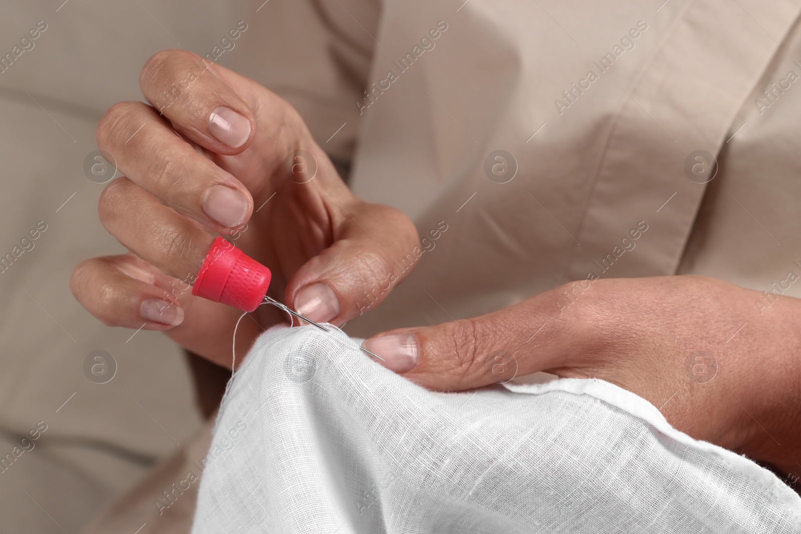 Photo of Woman sewing on white fabric with thimble and needle, closeup