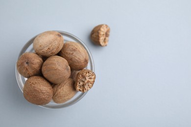 Photo of Nutmegs in glass bowl on white background, top view. Space for text