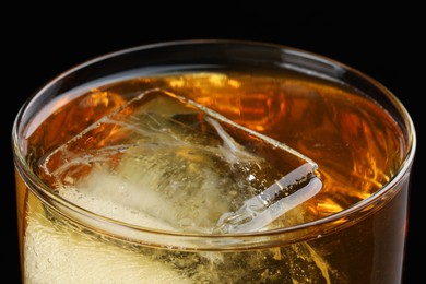 Tasty whiskey and ice in glass on black background, closeup