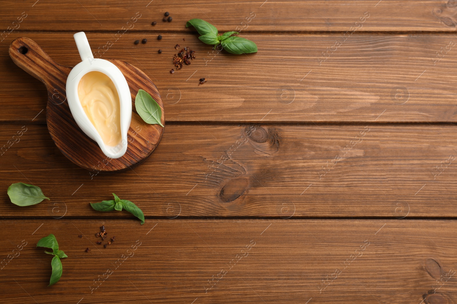 Photo of Tasty sauce in gravy boat, basil leaves and spice on wooden table, flat lay. Space for text