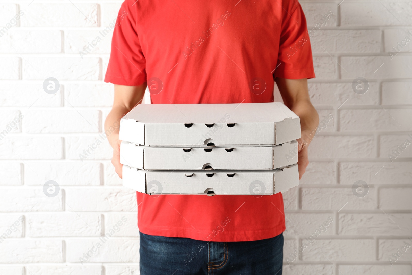 Photo of Young man with pizza boxes near white brick wall. Food delivery service
